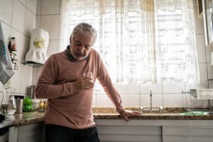 Man leans on the kitchen sink while holding a cup of water